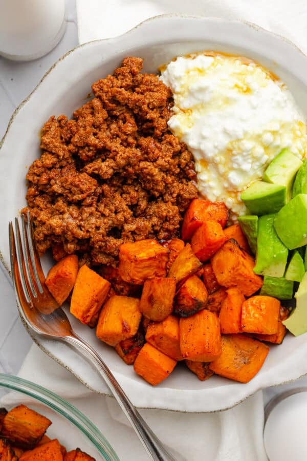 Bowl filled with cooked lean ground beef, cubed roasted sweet potato, avocado and cottage cheese.
