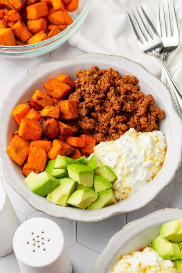 Viral ground beef sweet potato bowl with diced avocado and cottage cheese with forks next to it.