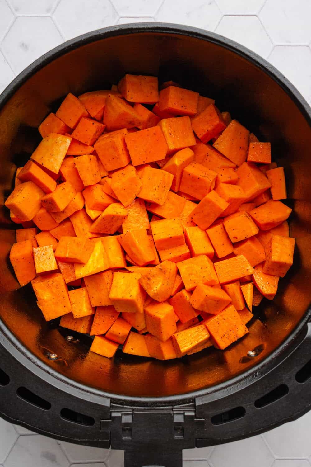 Seasoned uncooked sweet potato in an air fryer.