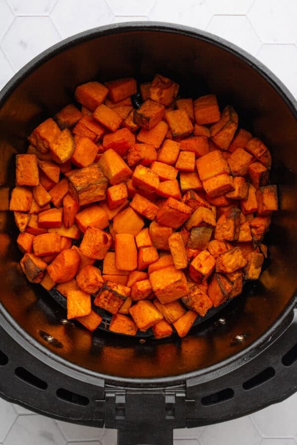 Air fried sweet potato cubes in an air fryer basket.