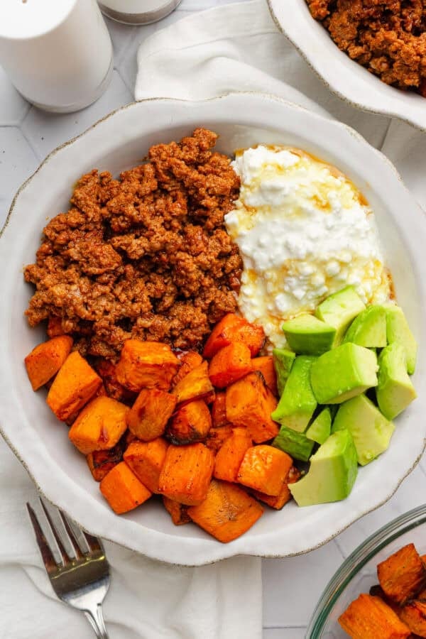 Beef taco meet, air fryer sweet potato cubes, avocado and cottage cheese in a bowl with a drizzle of honey on it.
