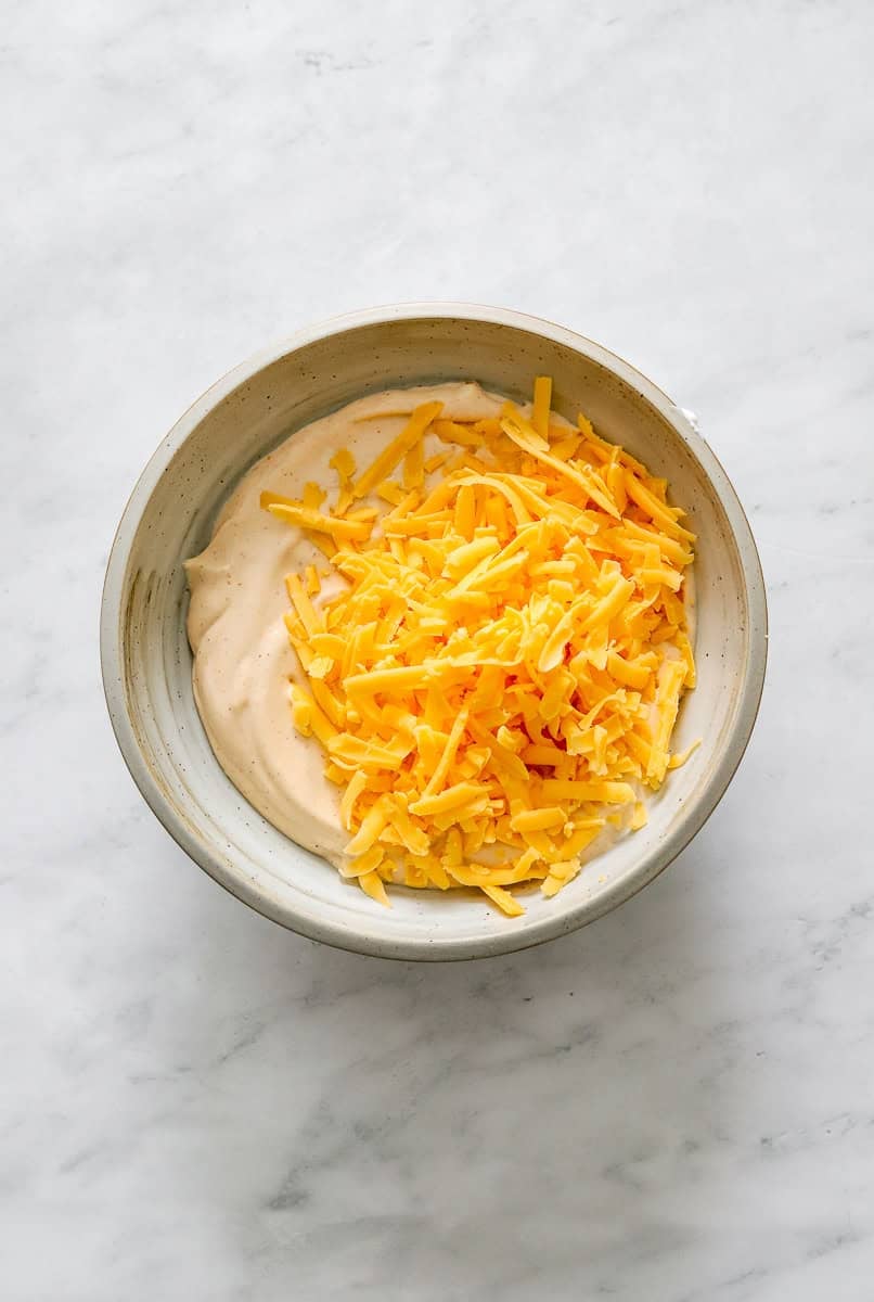 Blended cottage cheese and taco seasoning in a bowl with shredded cheddar on top of it.
