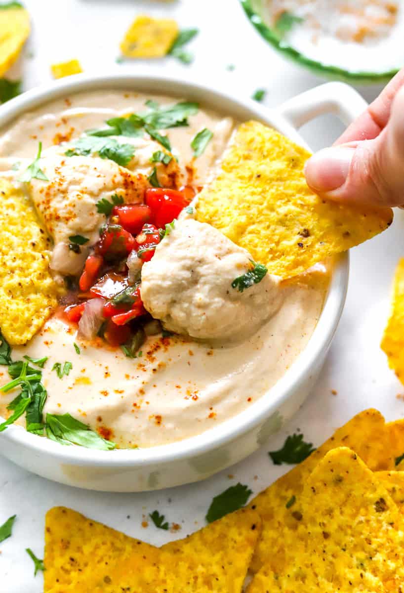 Hand dipping a tortilla chips in protein queso with cottage cheese.