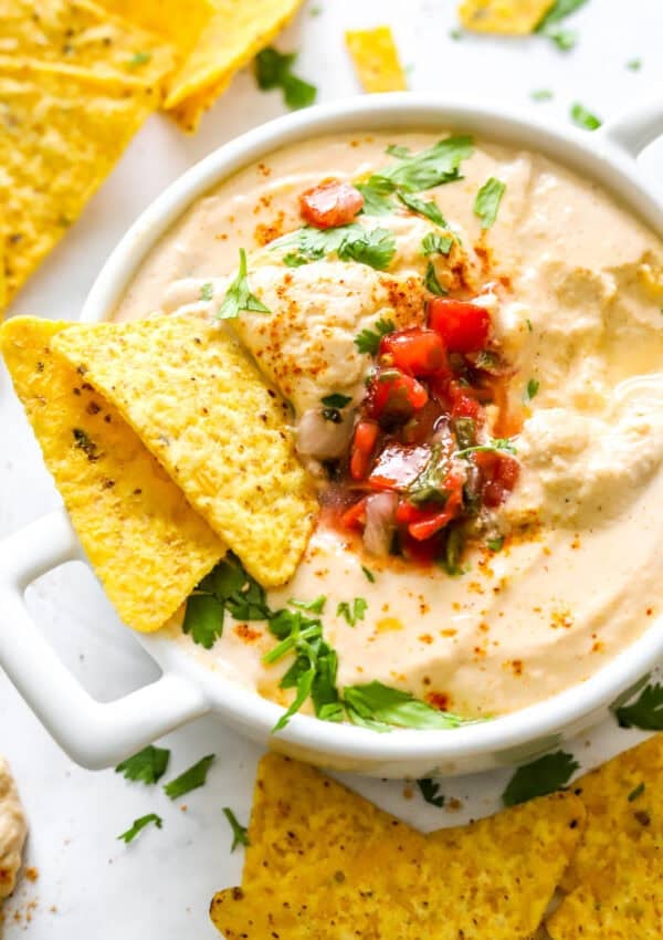 Cottage cheese queso dip in a dish toped with herbs and salsa with tortilla chips in the dish with it and around it.