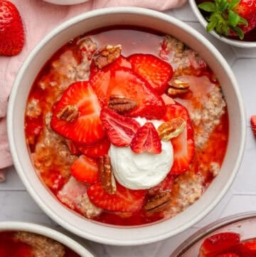 Cooked oats with strawberries in a bowls with more bowls of it around it.