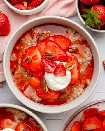 Cooked oats with strawberries in a bowls with more bowls of it around it.
