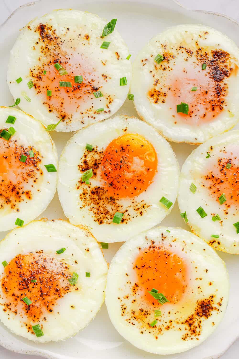 Plate of baked eggs with salt and pepper on top of them. 