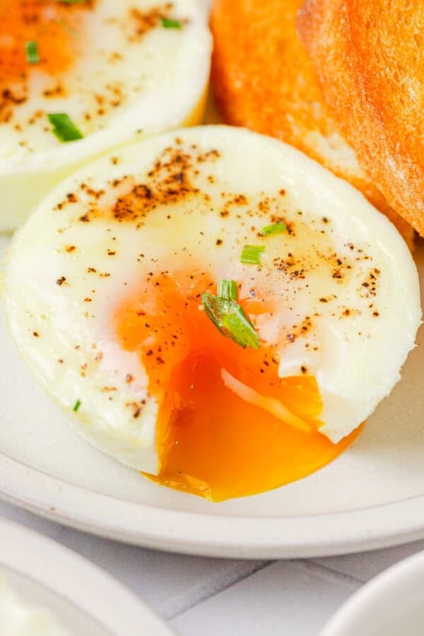 Baked egg cut open with yolk pouring out of it with more on the plate with it.