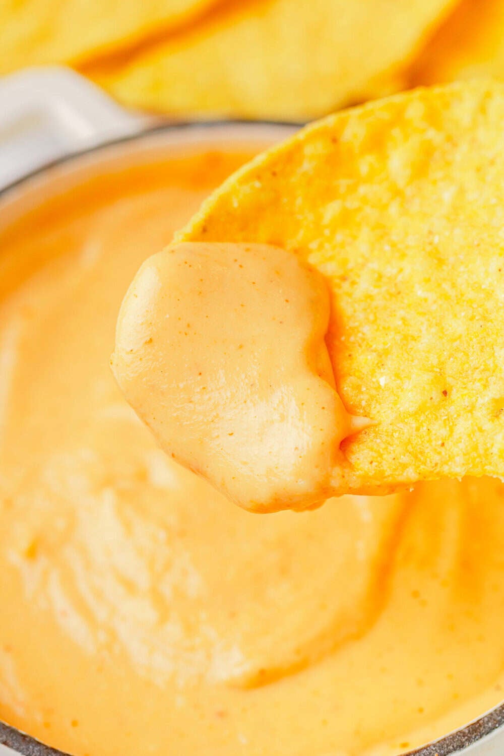 Protein cheese sauce in a bowl with a tortilla chip with sauce on it in front of it. 