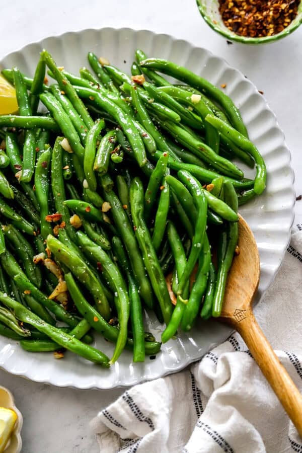 Platter of sauteed green bean with a wooden spoon on the plate.