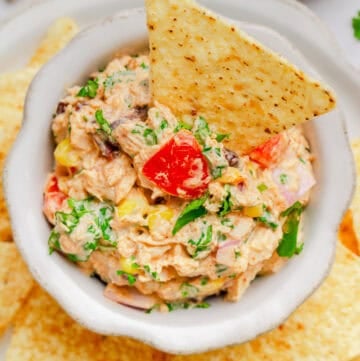 Mexican tuna salad in a bowl with a tortilla chip in it with more chips around it.