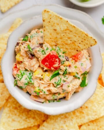 Mexican tuna salad in a bowl with a tortilla chip in it with more chips around it.
