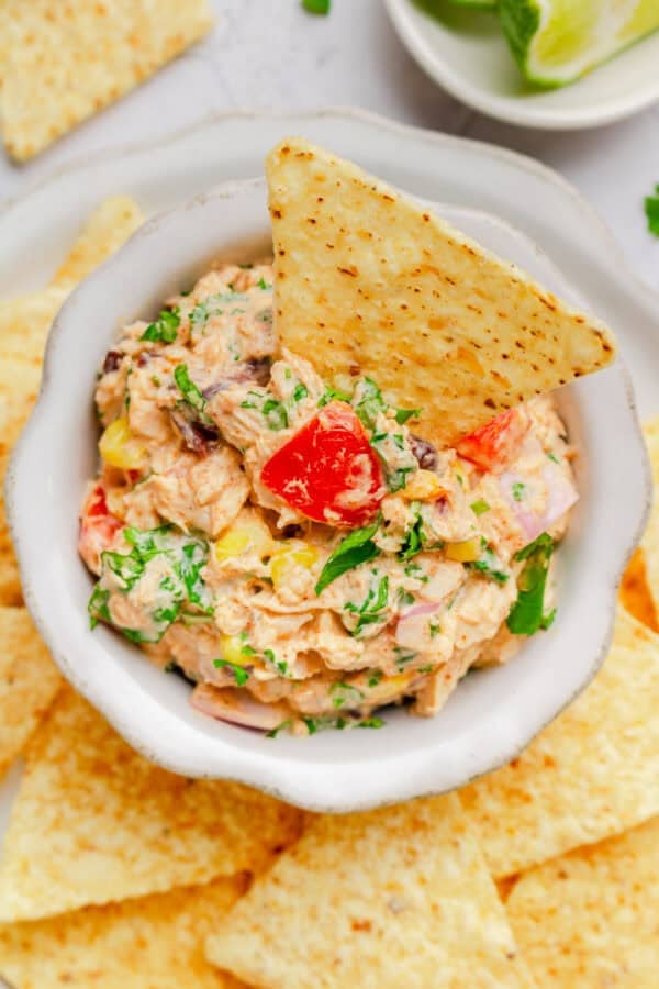 Mexican tuna salad in a bowl with a tortilla chip in it with more chips around it.