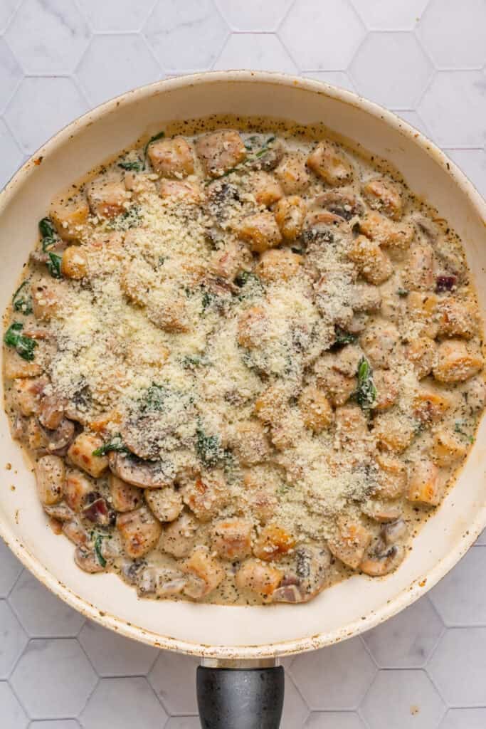 Creamy gnocchi in a pan topped with grated parmesan cheese. 
