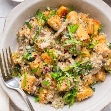 Trader Joe's cauliflower gnocchi in a creamy sauce in a bowl with green herbs on it with fork in the bowl with it.