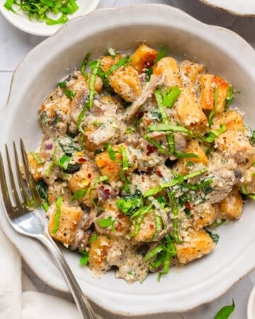 Trader Joe's cauliflower gnocchi in a creamy sauce in a bowl with green herbs on it with fork in the bowl with it.