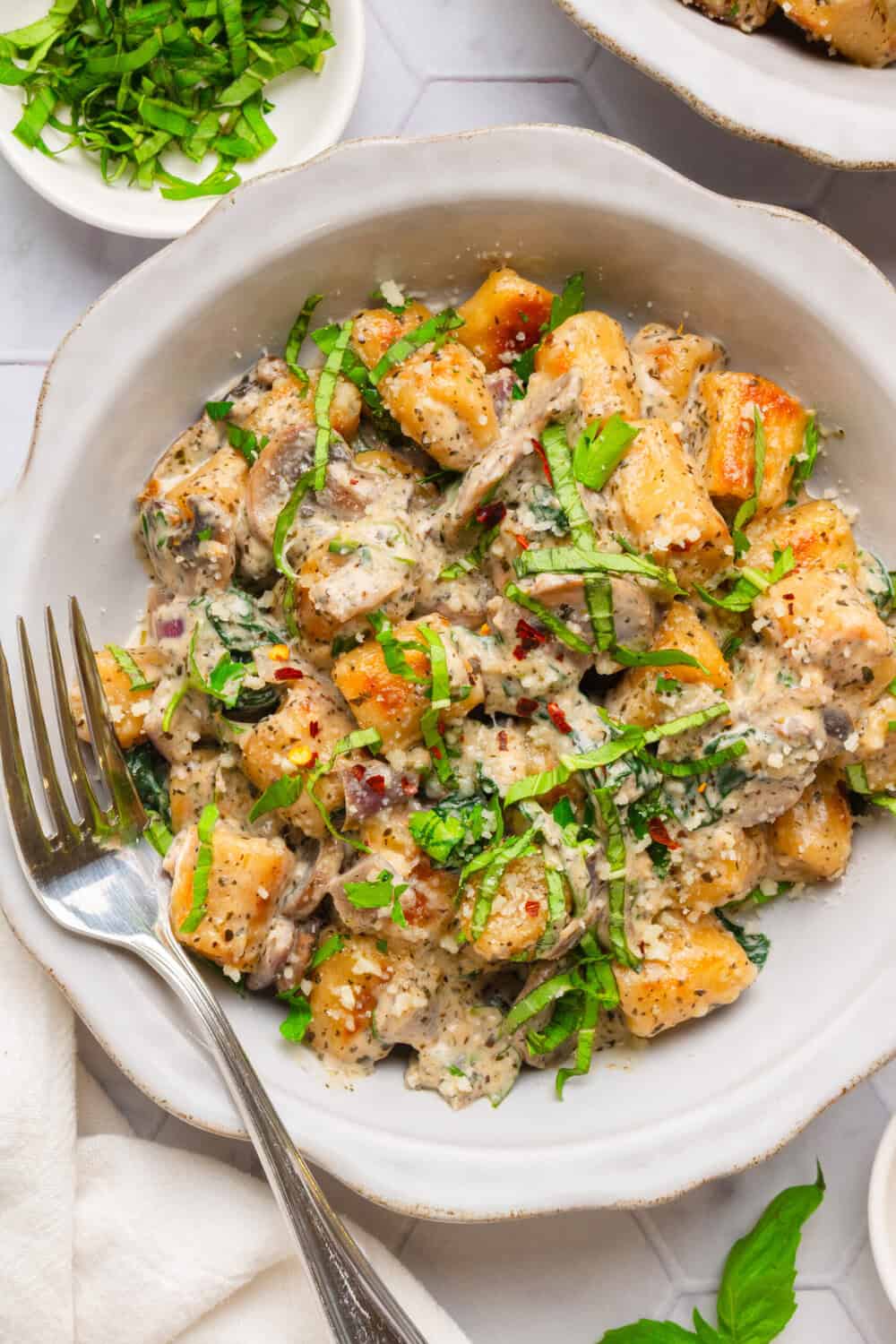Trader Joe's cauliflower gnocchi in a creamy sauce in a bowl with green herbs on it with fork in the bowl with it. 