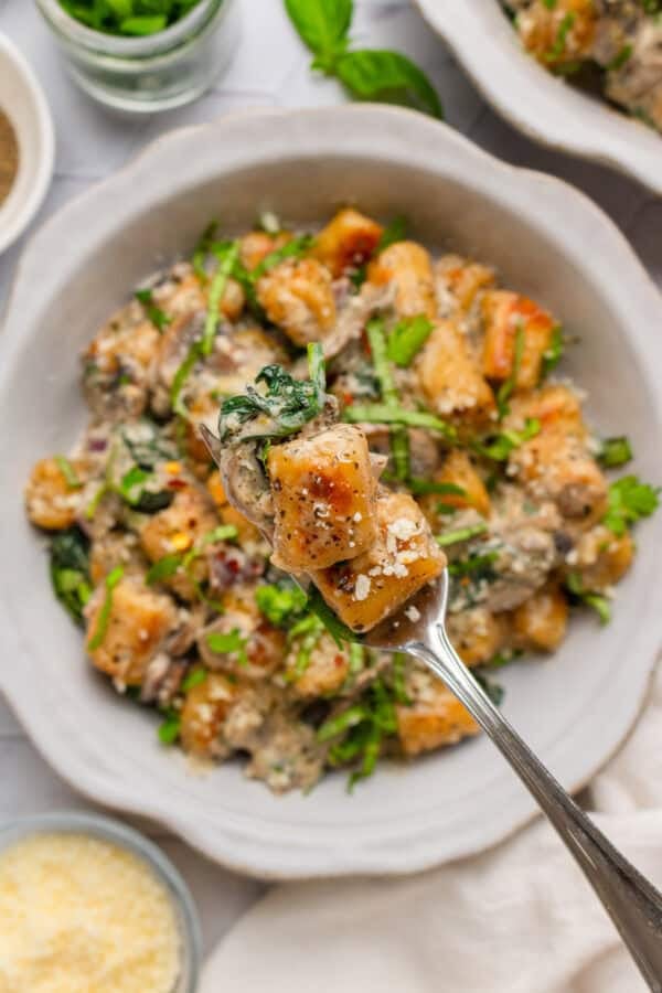 Fork with a piece of cauliflower gnocchi on it with a bowl of it behind it.