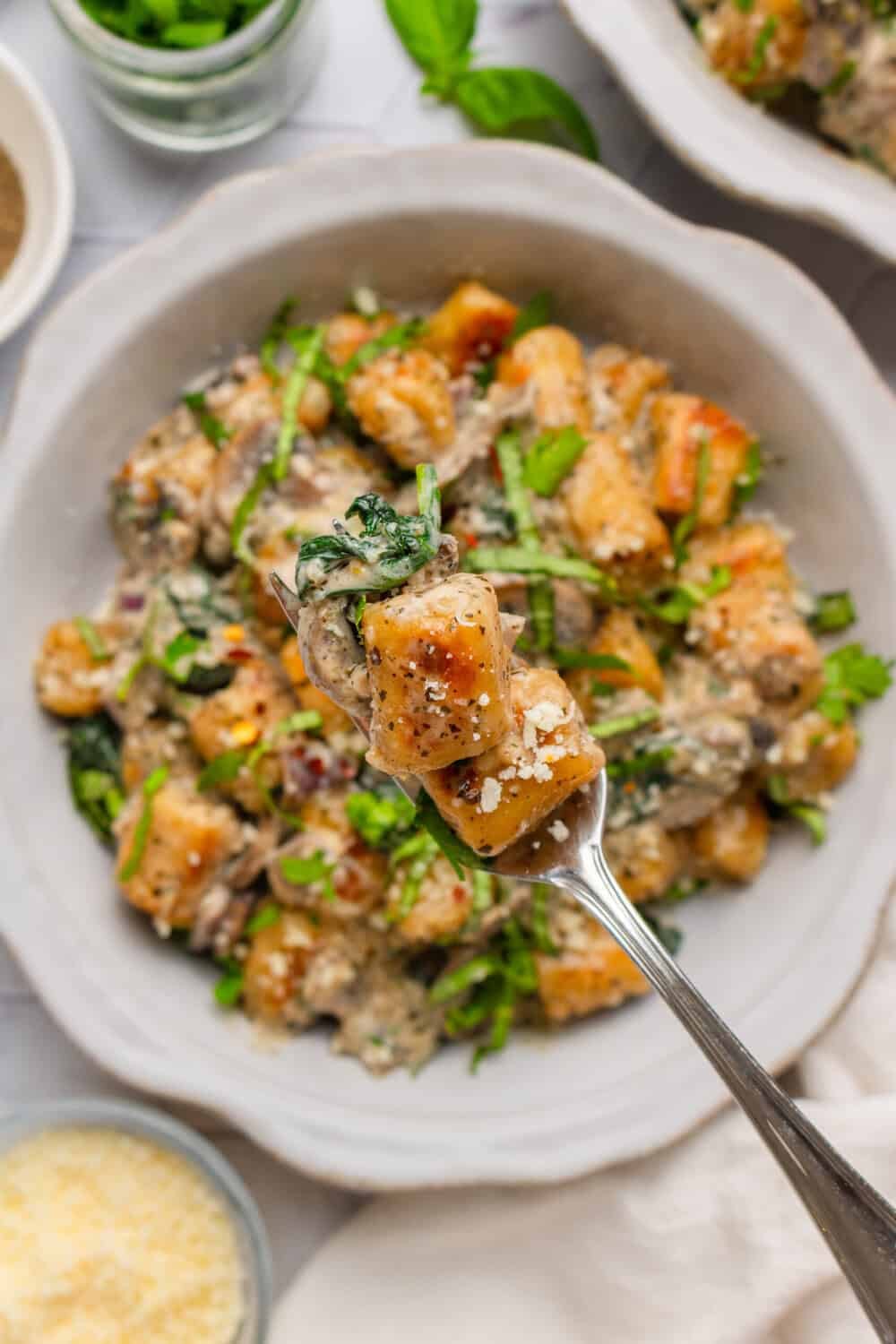 Fork with a piece of cauliflower gnocchi on it with a bowl of it behind it. 
