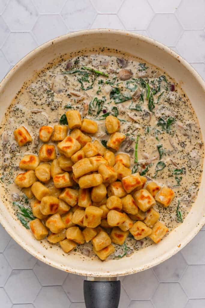 Creamy mushroom spinach sauce with cooked gnocchi on top of it in a pan. 