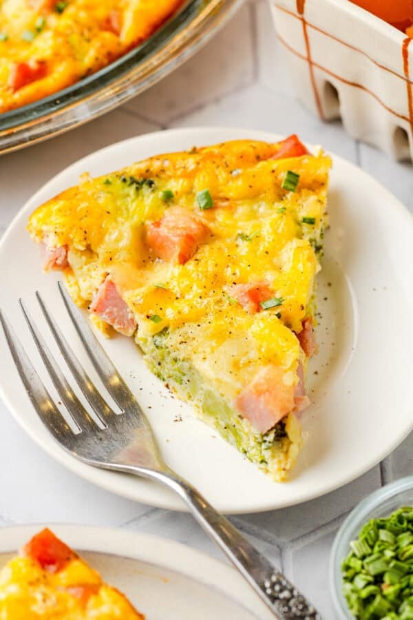 Plate with slice of broccoli ham crustless quiche with more behind it.