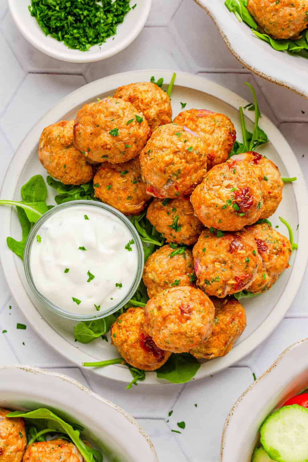 Plate of baked meatballs with Greek seasoning on top of green with a bowl of creamy dressing on the bowl with it. 