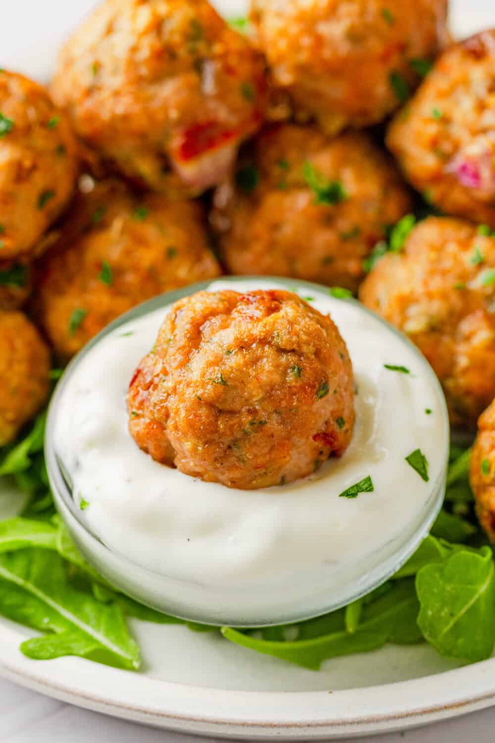 Close up shot of baked meatballs with one in tzatziki sauce with more behind it. 
