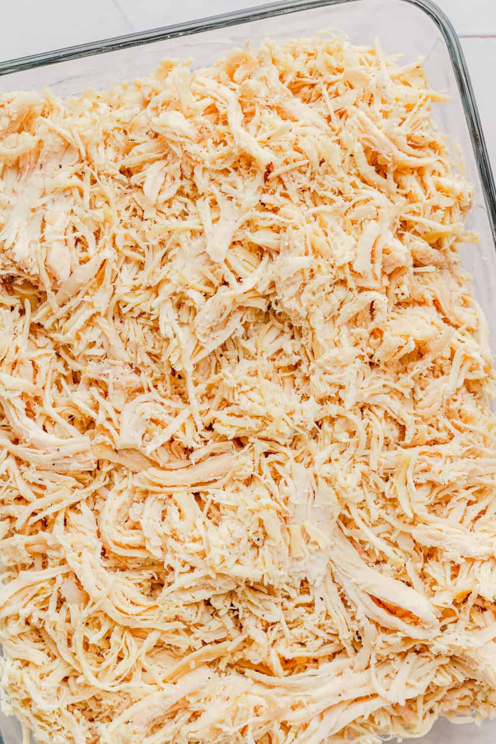 Cooked shredded chicken in a glass container. 