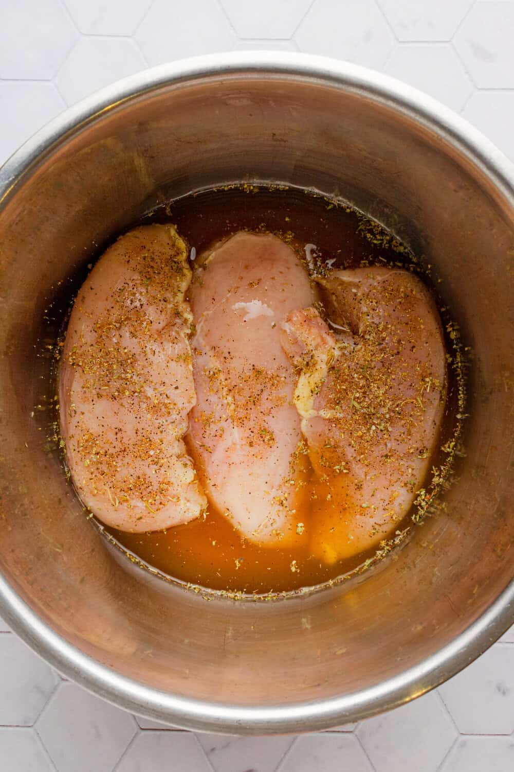Raw chicken breast in seasoning and chicken stock in an instant pot. 
