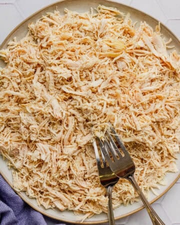 Round plate of cooked shredded chicken breast with two forks on the plate.
