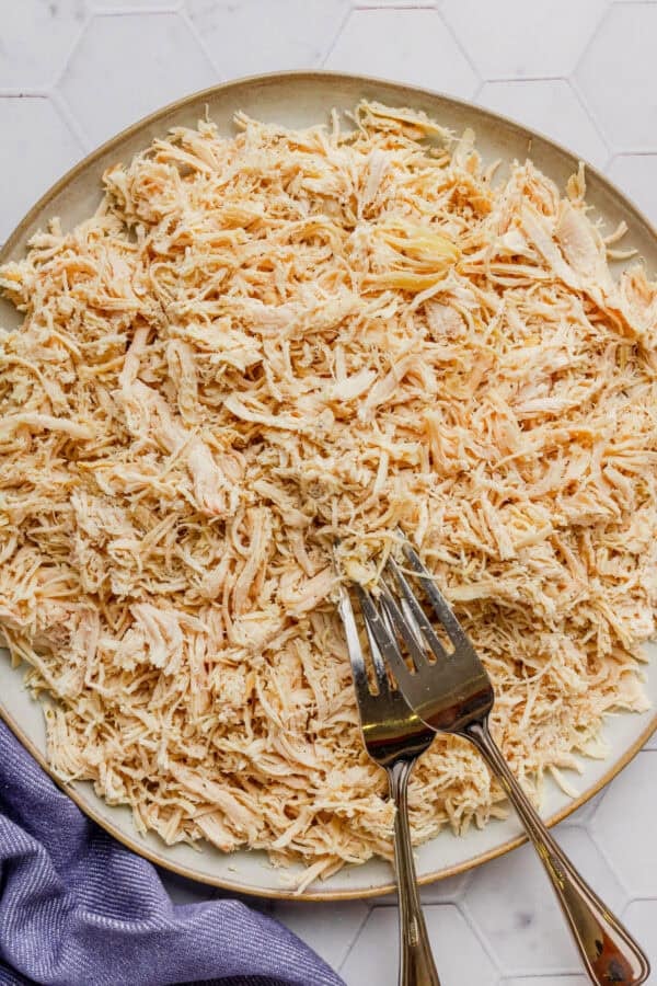 Round plate of cooked shredded chicken breast with two forks on the plate.