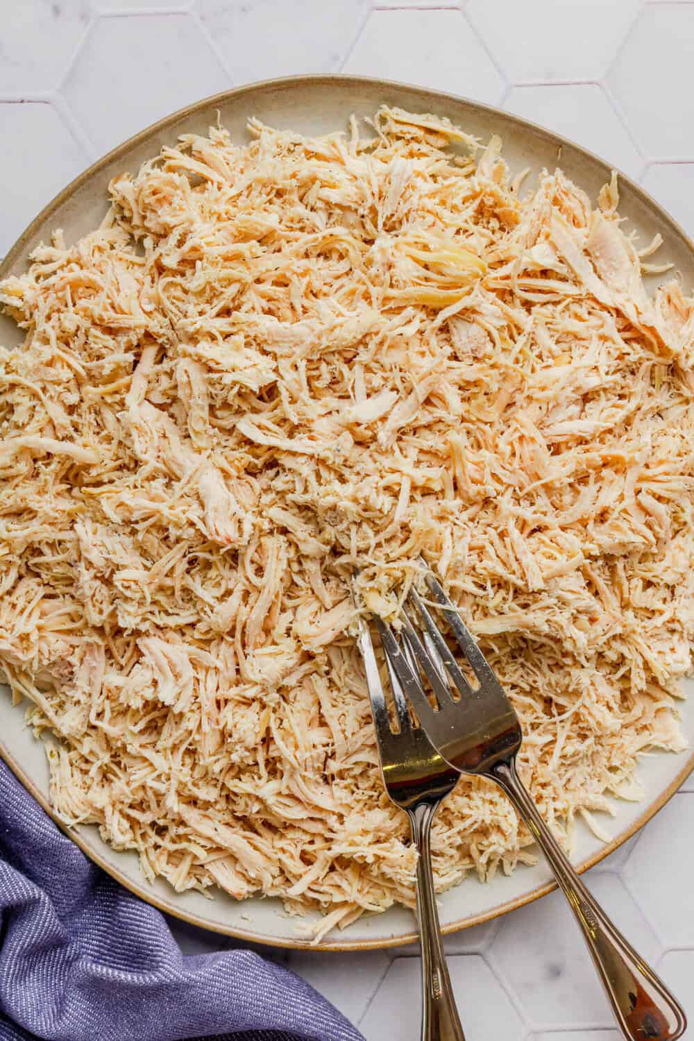 Round plate filled with Instant Pot shredded chicken breast with two forks on the plate with it. 