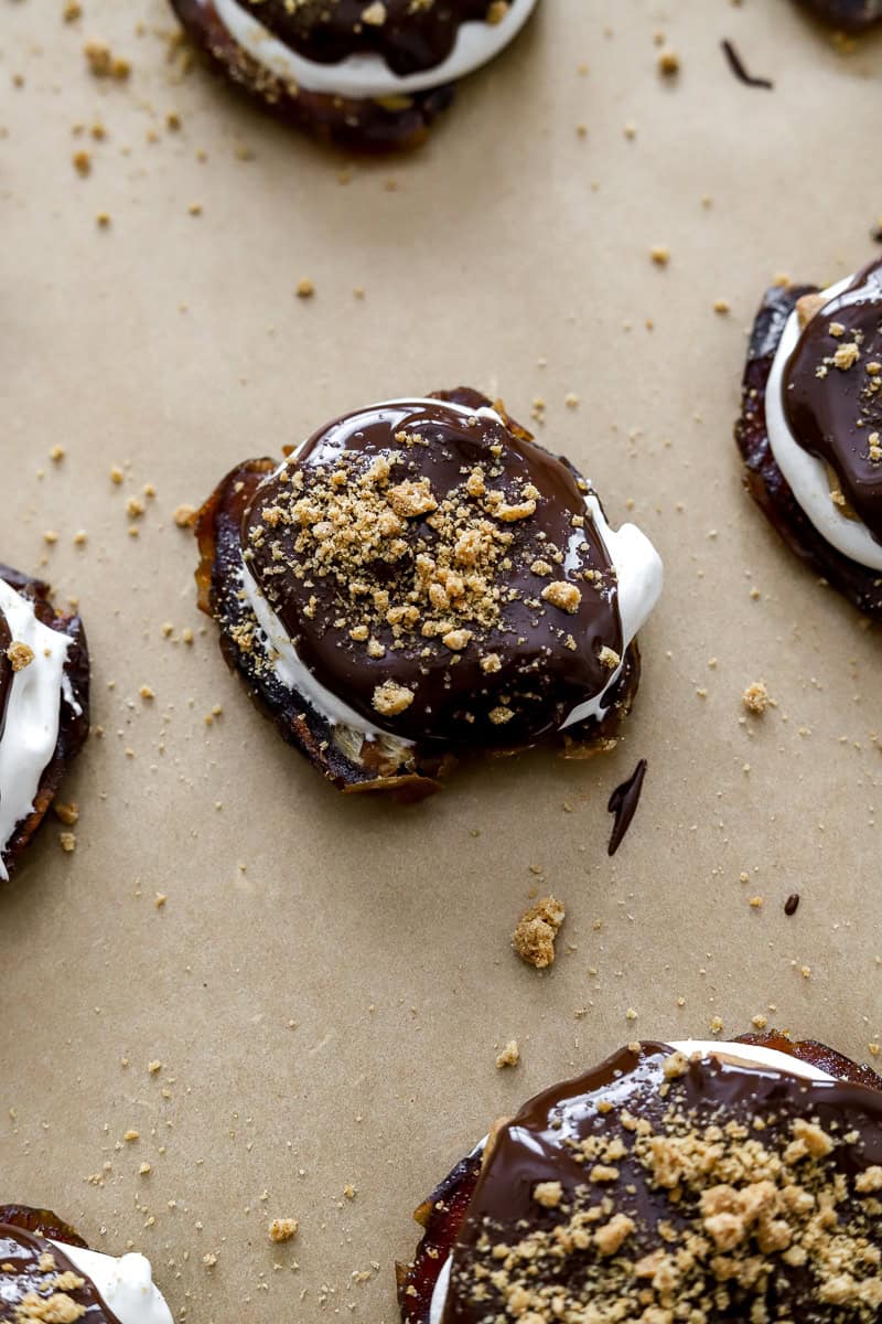 Smashed date with s'mores topping on a parchment lined pan with more around it.