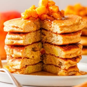 Apple cinnamon pancakes stack with a chunk cut out of it with cooked diced apples and syrup on top of it.