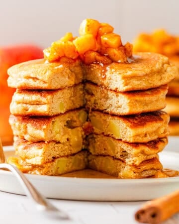 Apple cinnamon pancakes stack with a chunk cut out of it with cooked diced apples and syrup on top of it.