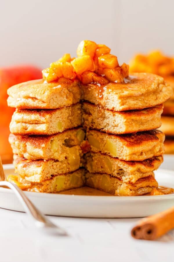 Apple cinnamon pancakes stack with a chunk cut out of it with cooked diced apples and syrup on top of it.