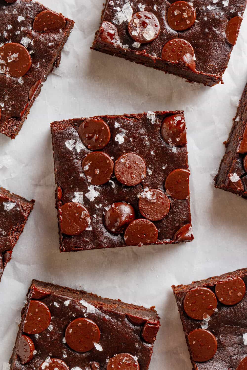 Chocolate avocado brownies with chocolate chips on top, cut into squares on top of white parchment paper.