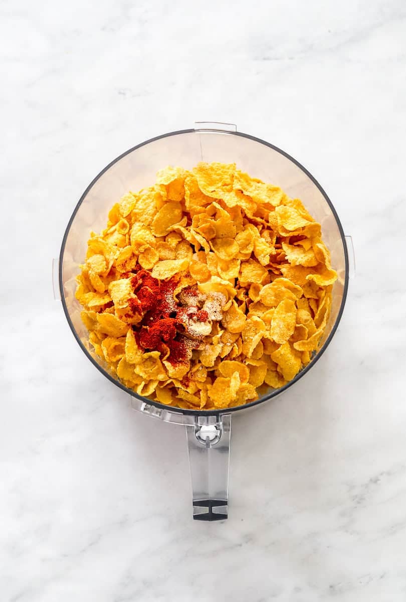 Cornflakes and seasoning in the bowl of food processor before being blended. 