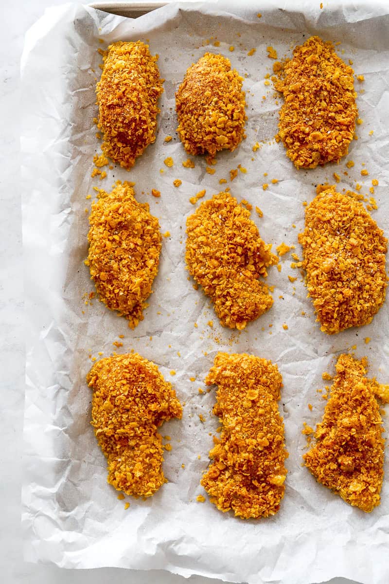 Lined pan with coated uncooked chicken on it. 