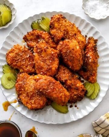 Air fryer hot honey chicken on a round plate topped with hot honey with more ingredient around it.