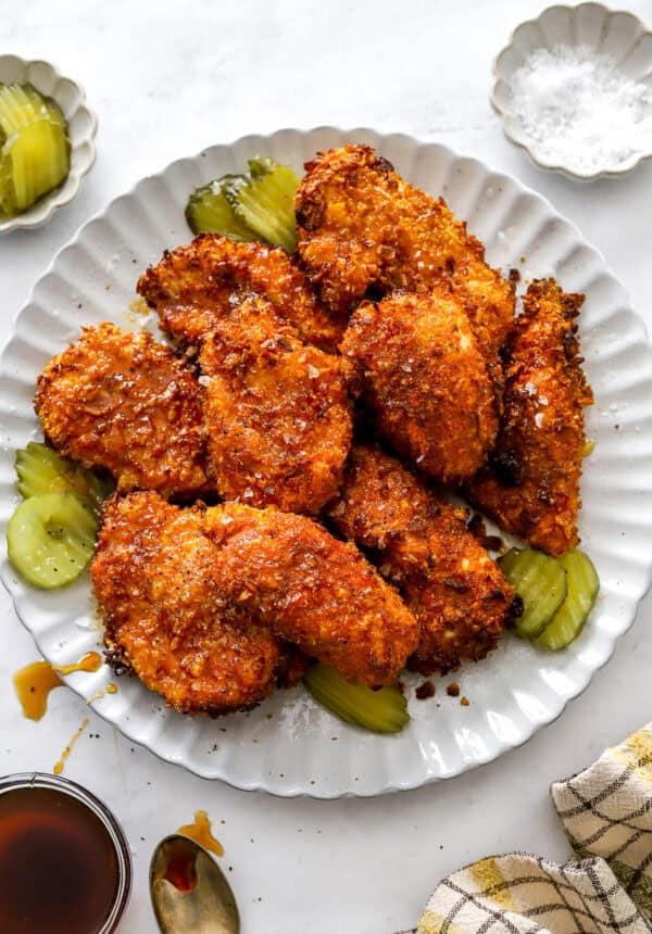 Air fryer hot honey chicken on a round plate topped with hot honey with more ingredient around it.