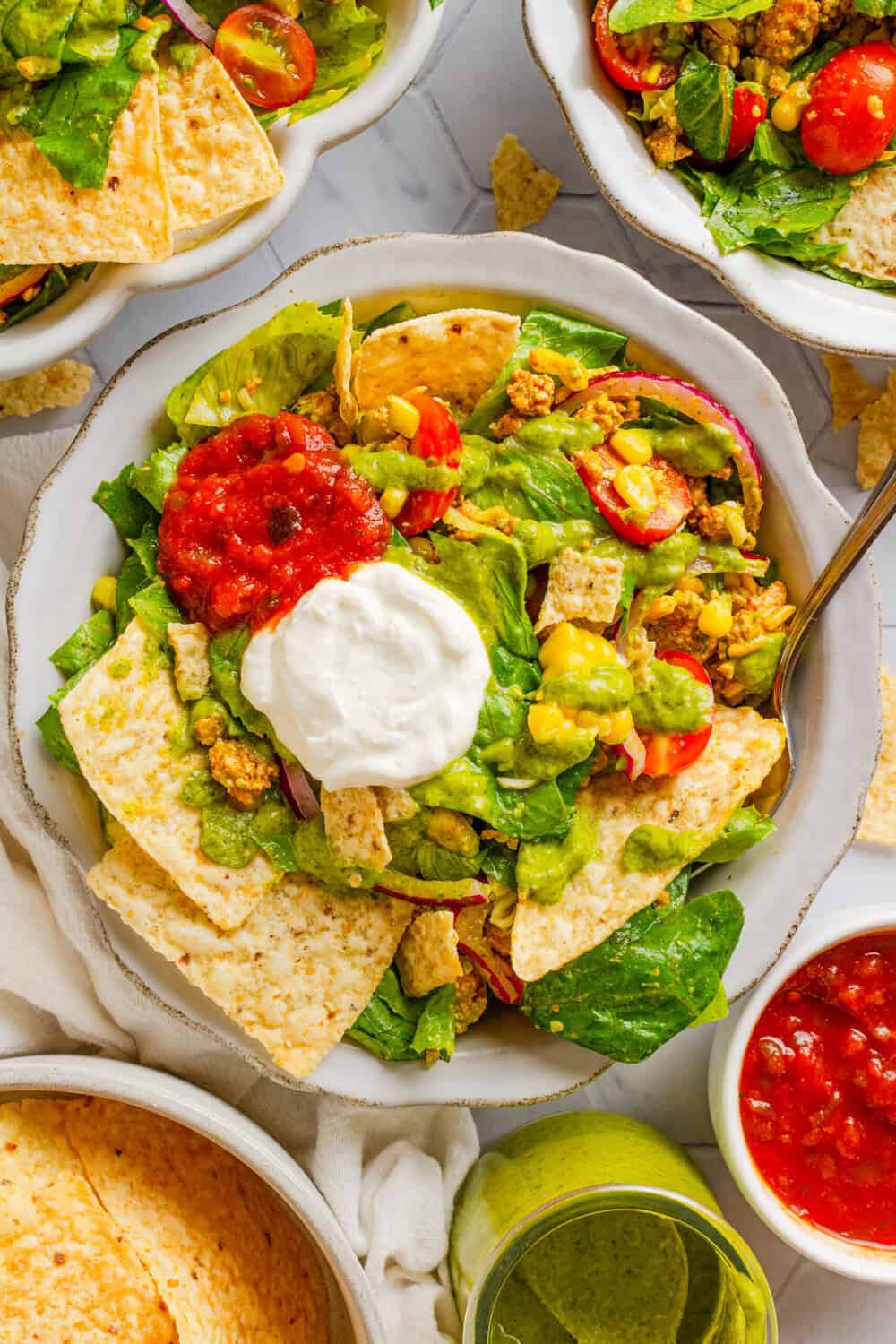 Ground chicken taco salad in a bowl topped with salsa and sour cream with more bowls of chicken salad behind it. 