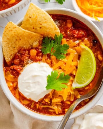 Bowl of instant pot turkey chili topped with tortilla chips, sour cream cilantro and melted cheddar cheese with a spoon in the bowl with it.