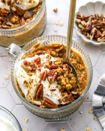 Round glass jar filled with pumpkin pie overnight oats with a spoon in the jar and more overnight oats behind it.