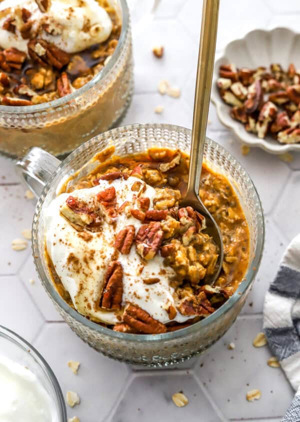 Round glass jar filled with pumpkin pie overnight oats with a spoon in the jar and more overnight oats behind it.