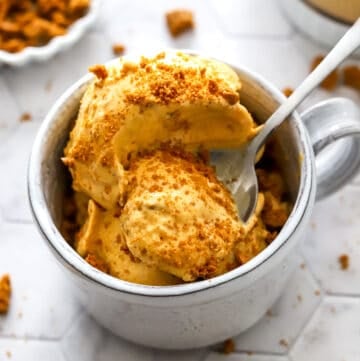 Mug filled with creamy pumpkin pie ice cream with crushed cookies on top of it with a spoon in the dish.