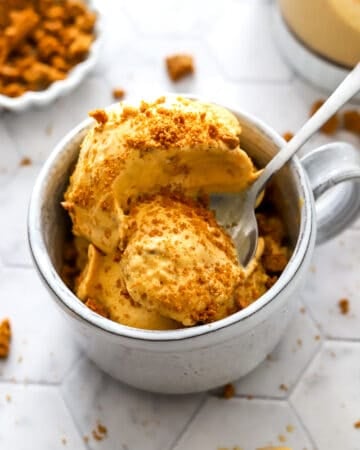 Mug filled with creamy pumpkin pie ice cream with crushed cookies on top of it with a spoon in the dish.