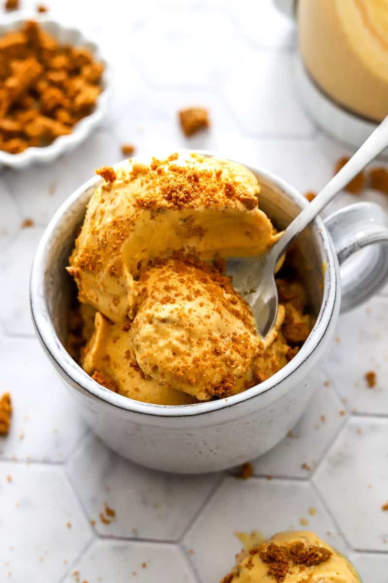 Mug filled with creamy pumpkin pie ice cream with crushed cookies on top of it with a spoon in the dish.