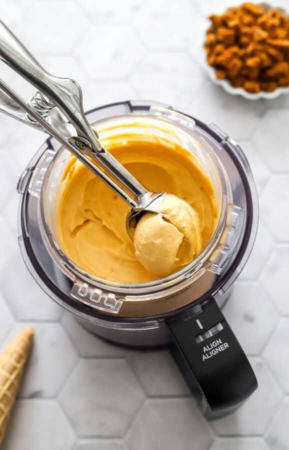 Blended Ninja Creami pumpkin yogurt protein ice cream in a Ninja container with an ice cream scoop in the container with it.