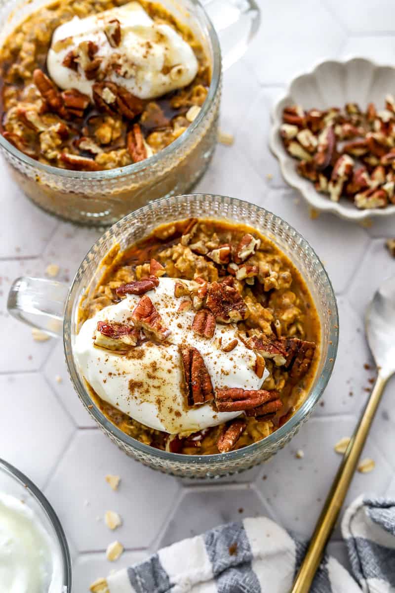 Two glass jars filled with chilled pumpkin overnight oats with greek yogurt and chopped pecans on top of each one. 